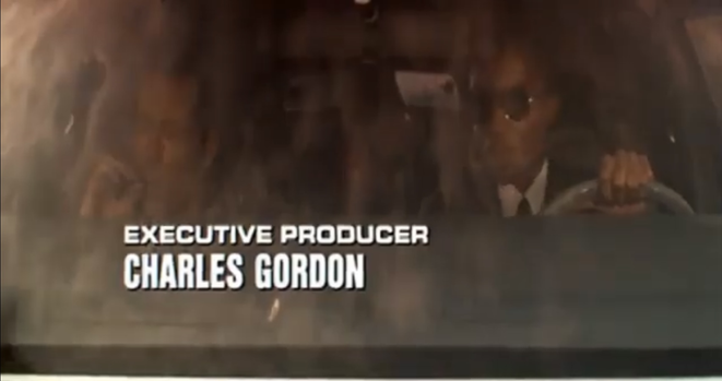 Screenshot from opening scene of DieHard, a famous Christmas Movie From the 70’s - John McLain and his friend are smoking a joint in the front seat of a car - in bold type the name Charles Gordon Executive Producer is written in white across the screen
