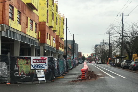 Construction site on the left, probably of commercial on the bottom and housing on 3 stories above. On the right is a walkway bordered by big orange barriers, a well marked bike lane, a car drive lane, and a car parking lane. There is enough room for large vehicles like construction trucks, emergency services, and buses to pass here, while still allowing people who walk, bike, and drive to move past this site. The construction is on North Williams Avenue.

Many cities have rules about access around construction sites. It seems like PDX usually enforces them.
