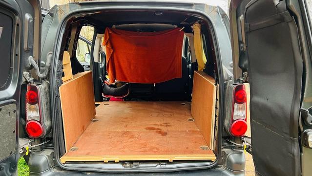 A small ply-lined van, from the perspective of the open rear barn doors