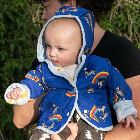 A baby wearing a quilt-coat that features zebras and rainbows