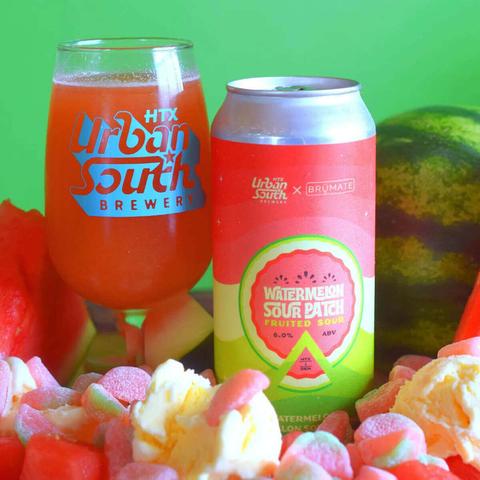 Glam shot of Urban South Brewery's Watermelon Sour Patch Fruited Sour Ale, with a can and glass of the beer sitting amongst a pile of fresh and candied fruit and fruit candies