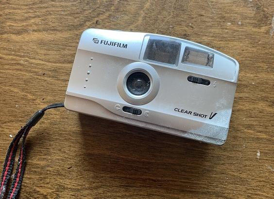 An old silver film camera with a red and black carry strap sitting on a wooden table.