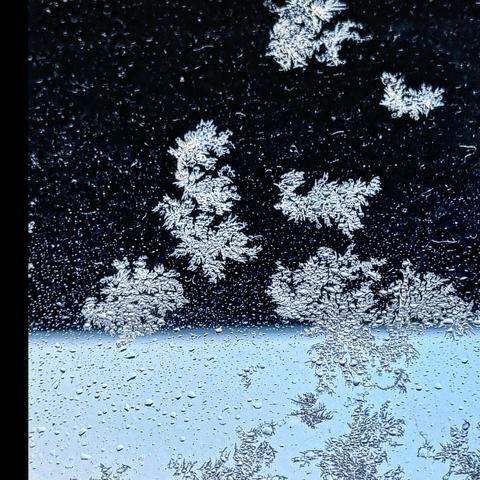 Feathery ice crystals growing across a window looking out onto a light blue frozen sky