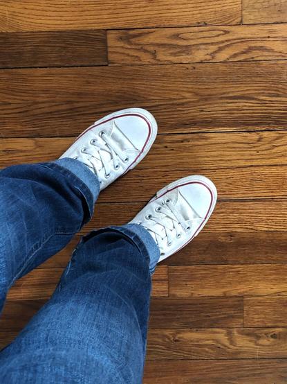 Top down view of white Converse on a blue jeans clad person standing on a hardwood floor