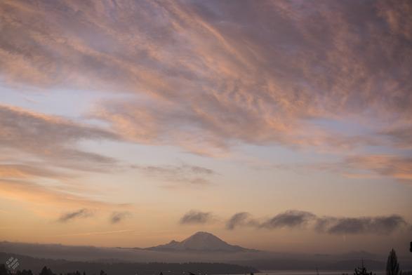 We're standing on a rise above the Lake looking south across Renton and other communities toward the Mountain. The sun is just coming up to our left, out of frame, and the mountinas is begiining to be lit, but the light is mostly in the clouds, which are purple lavender pink and peach. At ground level there is a thick bank of fog between us and the mountain. It's early enough that lights on the highway and cranes in the midground are still it.

Many First Nations share this area as it takes in quite a broad swath of Washington State.