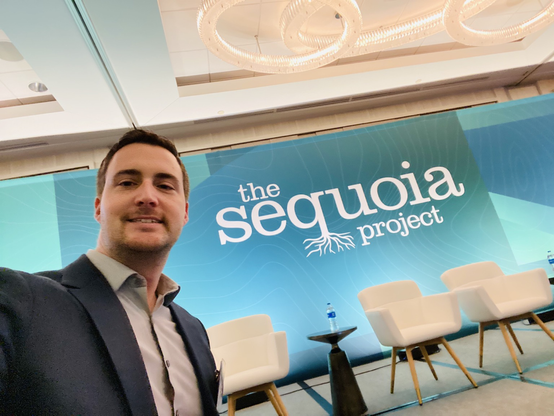 Man standing in front of stage with large banner reading “the Sequoia project”