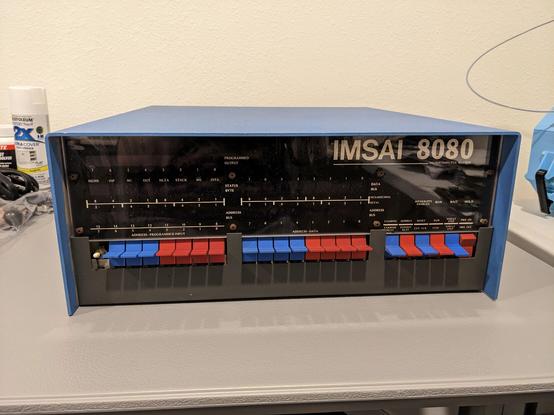 An IMSAI 8080 computer sitting on a grey plastic table.  The leftmost address switch is a plain white switch instead of the typical IMSAI blue paddle.