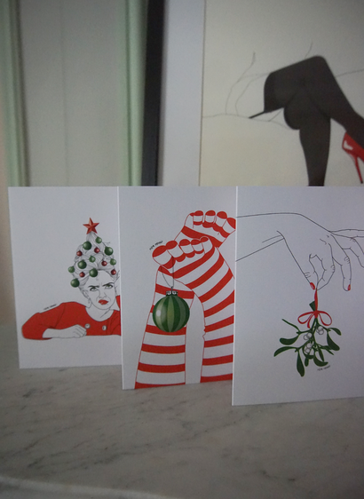 Photos de trois cartes de vœux illustrées posées sur une cheminée.
1. Une femme boudeuse avec une coiffure façon sapin de Noël avec plein de boules accrochées dedans
2. Une paire de jambes dressées en l'air vêtues de chaussettes de lutin rouges et blanches avec une boule Noël accrochée au gros orteil
3. Une main aux ongles vernis de rouge qui tient un petit brin de gui.