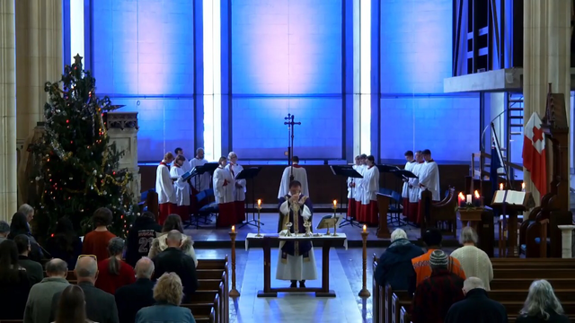 Priest holding up the elements at mass with purple lit sanctuary in the background