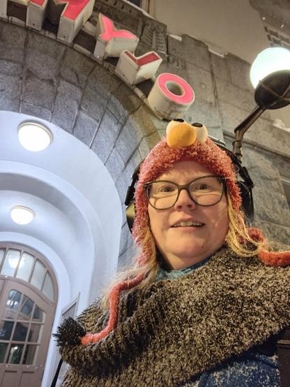 Low angle selfie, showing me in front of the doorway to the concert venue. I'm dressed in peacock blue coat, dark scarf and an Elmo from Sesame Street hat. Everything is lightly covered in snow.