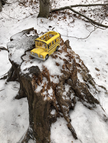 A toy yellow school bus sitting on a tree stump in winter