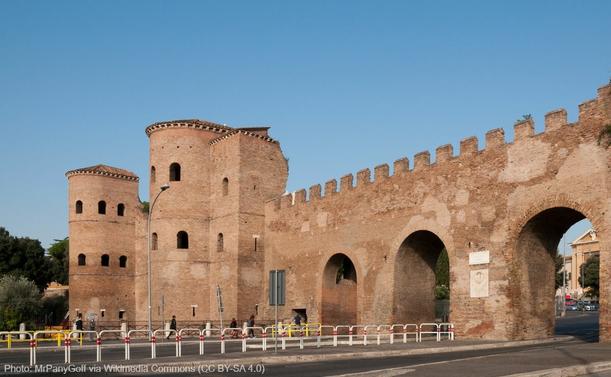 The photo shows a section of the Aurelian Wall in Rome. Modern streets lead through three round arches. To the left is a Roman city gate, the Porta Asinaria. Photo: MrPanyGoff via Wikimedia Commons (CC BY-SA 4.0)