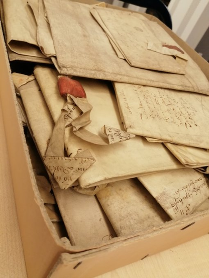 A storage box of a miscellaneous pile of medieval and early modern charters, with one attached red seal visible