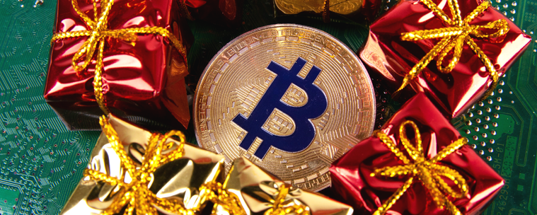 A physical representation of a Bitcoin surrounded by wrapped Christmas presents on top of a green circuit board.