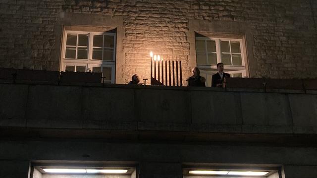 Bild zeigt den Balkon des Rathauses bei Dunkelheit. In der Mitte steht ein Hannuka-Leuchter, an dem drei Lichter leuchten.