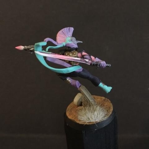 A miniature female aeldari harlquin for the warhammer 40k game. Painted with pink and purple check marks. Rear view, a power sword visible in the hand with color fading from white to vibrant pink to a dark purple.