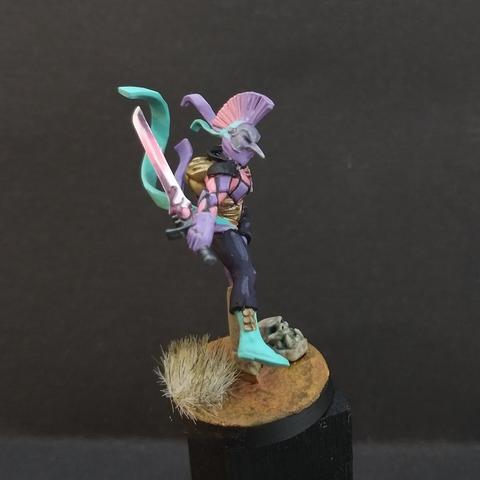 A miniature female aeldari harlquin for the warhammer 40k game. Painted with pink and purple check marks. Side view.