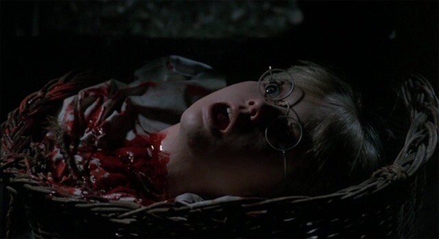 A blonde bespectacled boy’s severed head lays on the floor with his eyes and mouth agape