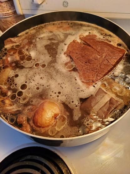 Pot of pho soup broth with beef flank on white stovetop.