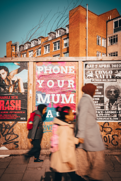 A mom and her children walk by a poster that says 'phone your mum'
