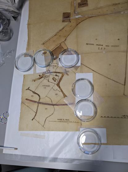 Yellowed tracing paper with layers of release paper and blotter beneath round glass weights.