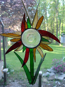 A 3D glass, flower with red, orange and gold narrow, pointed petals radiating out from a clear, textured glass rondel.