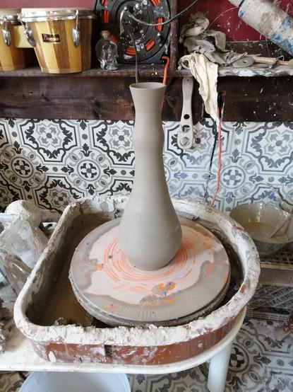 Pottery wheel with freshly thrown tall vase that tapers upwards.