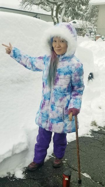 Standing behind family sedan, fully covered with snow to show how much accumulated in 24 hrs.  I'm wearing a tie dye puffy parka, holding a cane in my left hand & pointing to the snow on car with right hand.