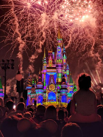 Cinderella castle at Disney World with colorful light projections during fireworks show.