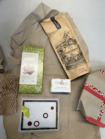 A collection of gifts: chocolate, coffee, locally made soap, an enameled pin of a native NZ moth made by a local artist on a print by Julian Dashper.