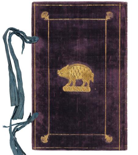 Front cover of the book, in a regal purple velvet with a stamp showing a large golden foiled boar facing to the spine, surrounded by other gold details. A pale blue-green ribbon holds the spine together on the left