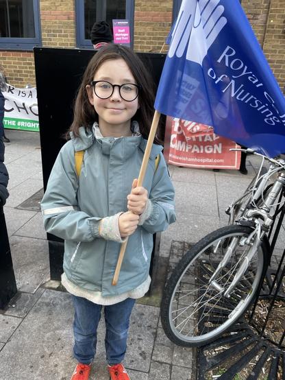 A child with a Royal College of Nursing flag and some strike banners behind him.