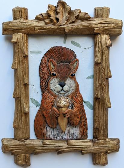 A three-dimensional clay squirrel, holding a gold acorn on a white background embedded with small green leaves, within a hand-carved vintage frame designed to look like branches with carved acorns on top, like a crest.