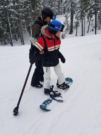 On a snowboard, holding on outrigger ski pole & my instructor is holding my my waist.