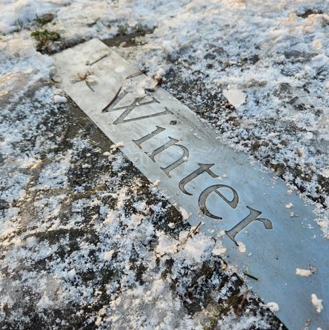 A metal strip, surrounded by snow and ice, with an engraving that reads "Winter"