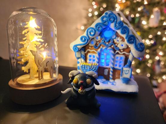 A trio of little decorations. A baby Krampus, a Gingerbread Hanukkah house and a glass dome containing a woodcut for tree and reindeer with tiny led lights.