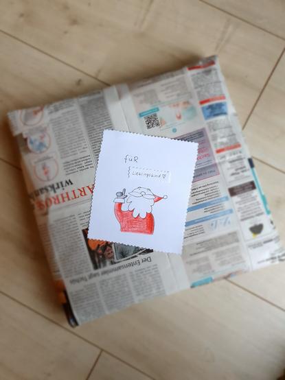 In Zeitungspapier verpacktes Geschenk. Darauf klebt ein Bild mit einem gezeichneten Weihnachtsmann und der Aufschrift "für Lieblingskind"