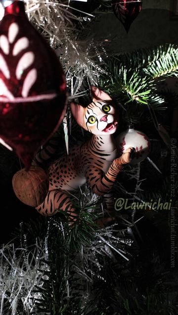 An articulated Savannah cat doll playfully eyeing Christmas decorations in a tree