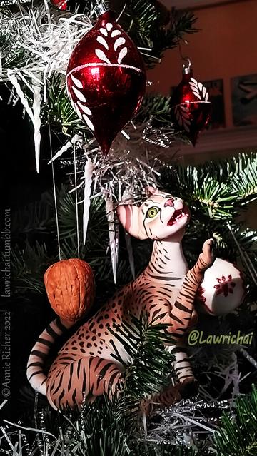 An articulated Savannah cat doll playfully eyeing Christmas decorations in a tree