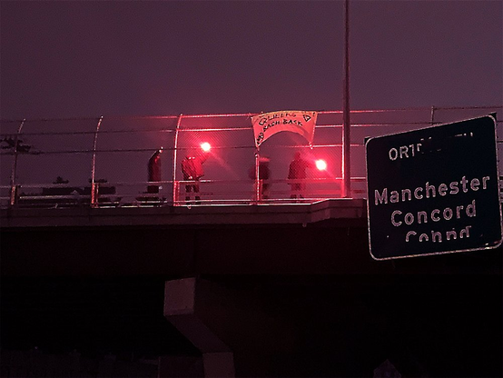 FAS comrades stand by with flares on an overpass after hanging a banner that says "We defend us! Queers bash back!"