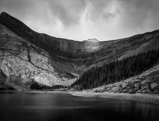 Alpine lake flanked with shadow filled wall of nearb Mount Bryant. One spot light from the sun breaking through storm clouds.