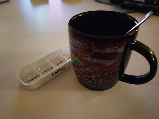 Pillendose für Freitag und ein Pott Kaffee mit Bayern München Stadion drauf, auf einen weißen Tisch