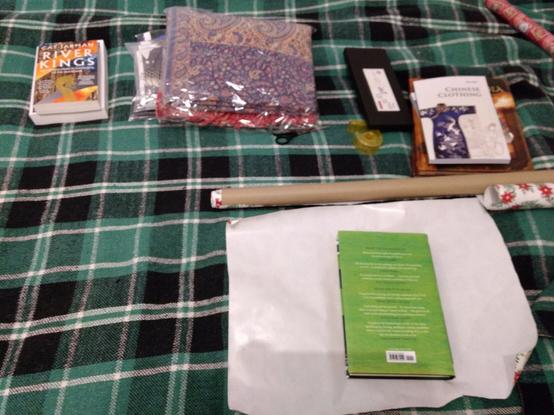 A green and white tartan blanket on which there are books, a shawl, and a new set of chopsticks, some Christmas giftwrap, scissors and scotch tape, all set and ready to go!