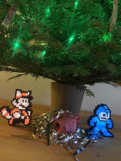 Irgendwie ein Krippenszenario:  Mario und Megaman-Pixelartlampen flankieren ein Quietscheschwein gebettet auf silber Lametta