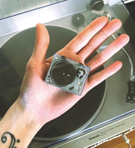 A miniature Technics turntable sits in the palm of the hand. Full size turntable in the background.