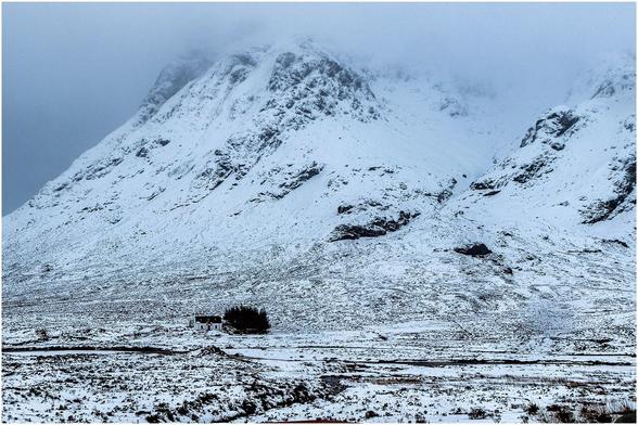 Isolated cottage beneath an imposing snow covered mountain.