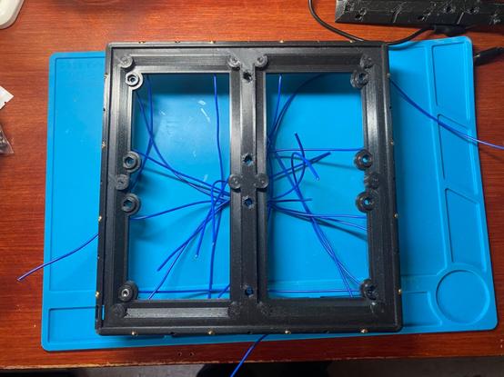 A black 3D printed frame with gold metal touch points around the edges and blue wires coming from each one. The other end of the wires are not yet connected to anything.