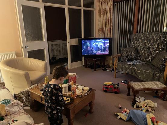 Malc eating at a cheeseboard on a coffee table with Muppet Christmas Carol playing on TV in front of him