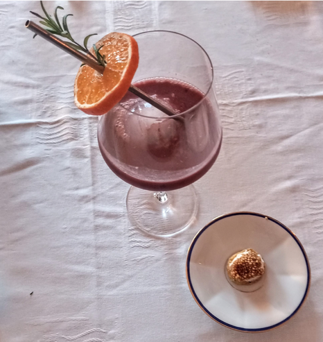 Ein Weinglas mit einem alkoholfreien Cocktail - sieht aus wie Rotwein. An dem Strohhalm steckt eine Orangenscheibe mit einem Rosmarinzweig.
Auf einem kleinen Teller ein kleiner Gruß aus der Küche - auf einem Parmesankeks etwas Mascarpone und Senfkörner-"Kaviar"