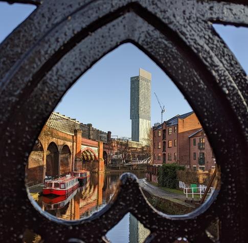 Iconic Beetham Tower building and rail bridges near the Bridgewater Canal as seen through a heart-shaped gap in a footbridge over the canal in Manchester, UK.